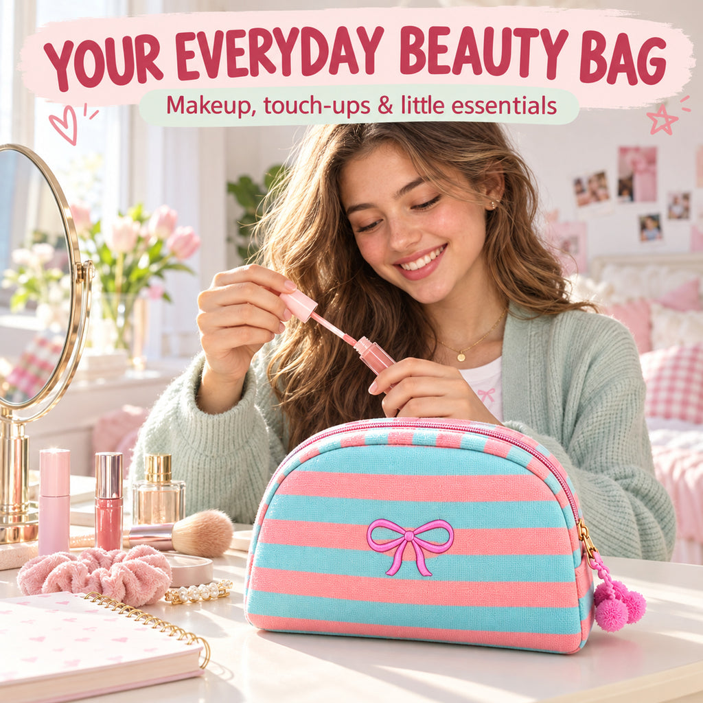 Model at a vanity with an Aqua and Coral striped makeup bag featuring a pink bow embroidery and pom-pom zipper charm. Styling props are not included.