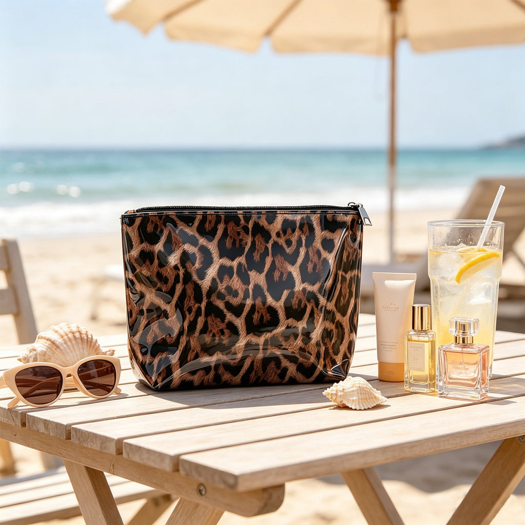 Caramel brown leopard print PVC makeup bag on a beachside table with sunglasses, seashells and beauty essentials. Styling props are not included.