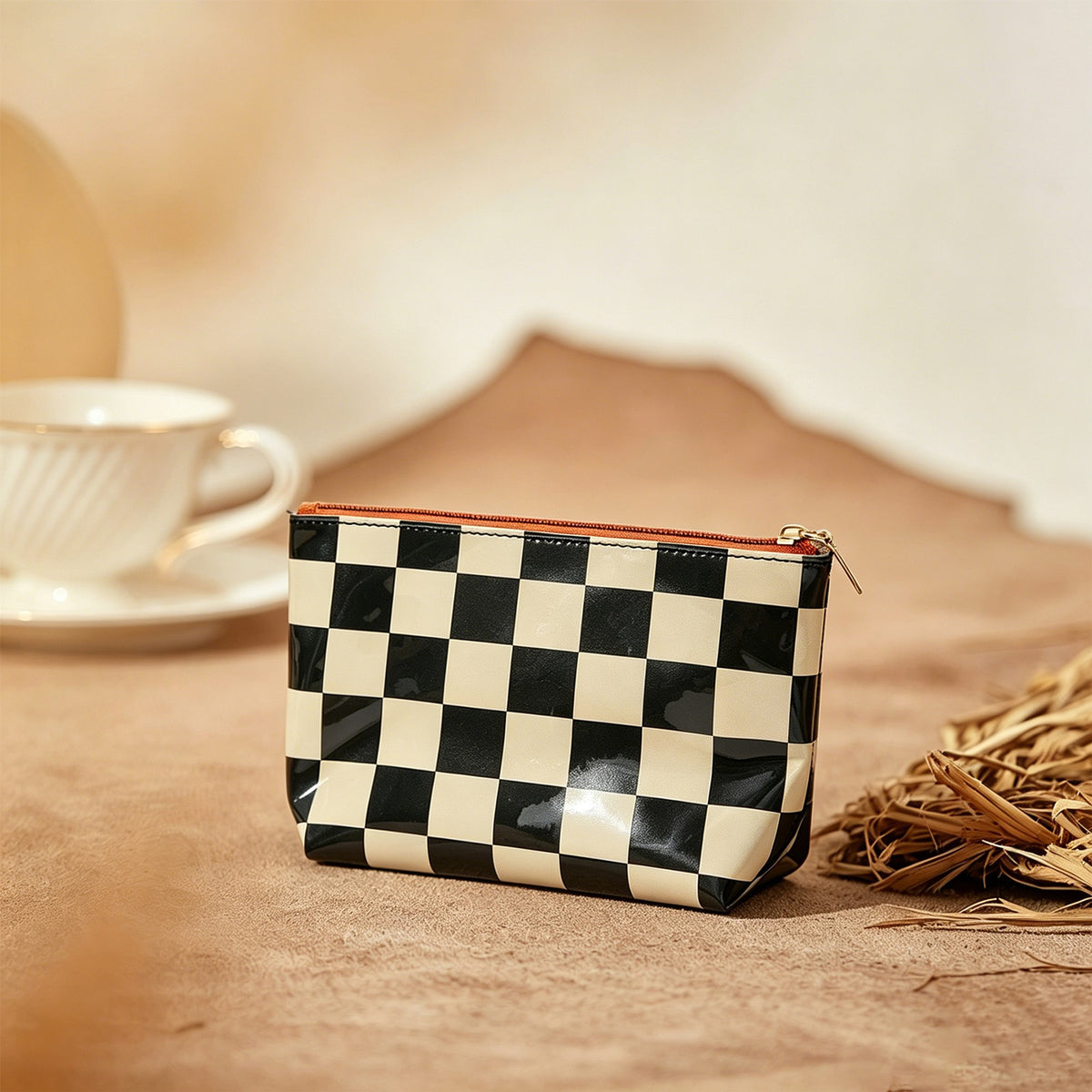 Black and Cream checkerboard PVC makeup bag with a rust-colored zipper, styled beside a coffee cup on a warm neutral tabletop. Styling props are not included.