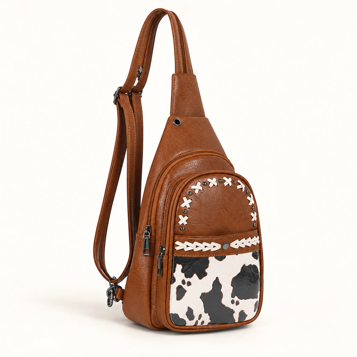 Cognac Brown convertible sling bag with white lacing, dark studs and a black, charcoal and off-white cow-print front panel.