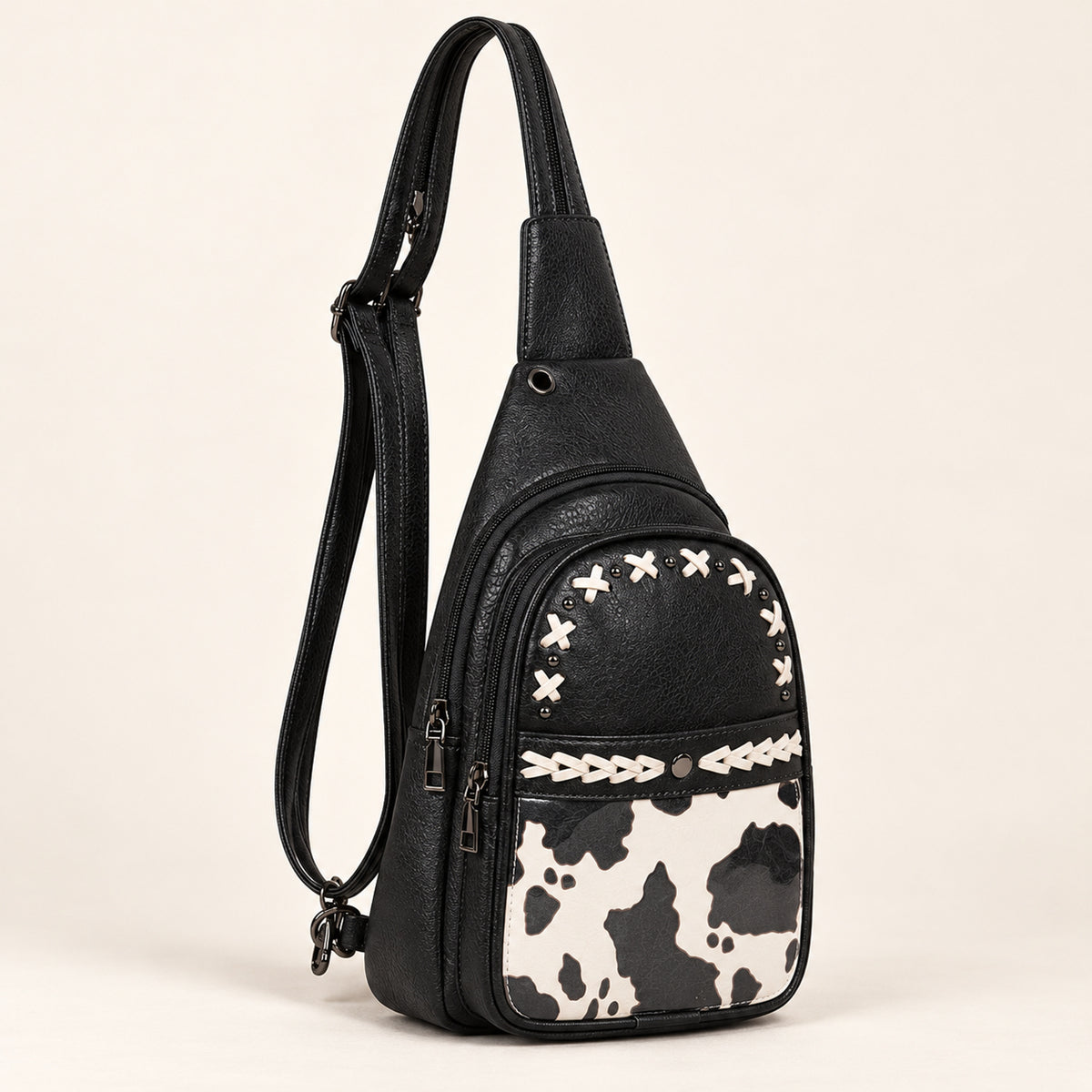Black convertible sling bag with white lacing, dark hardware and a black, charcoal and off-white cow-print front panel.